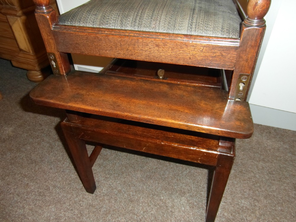 An antique Georgian mahogany childs high chair featuring a carved pierced splat back, wooden safety bar, upholstered seat, and integrated footrest on a wooden stand. View II