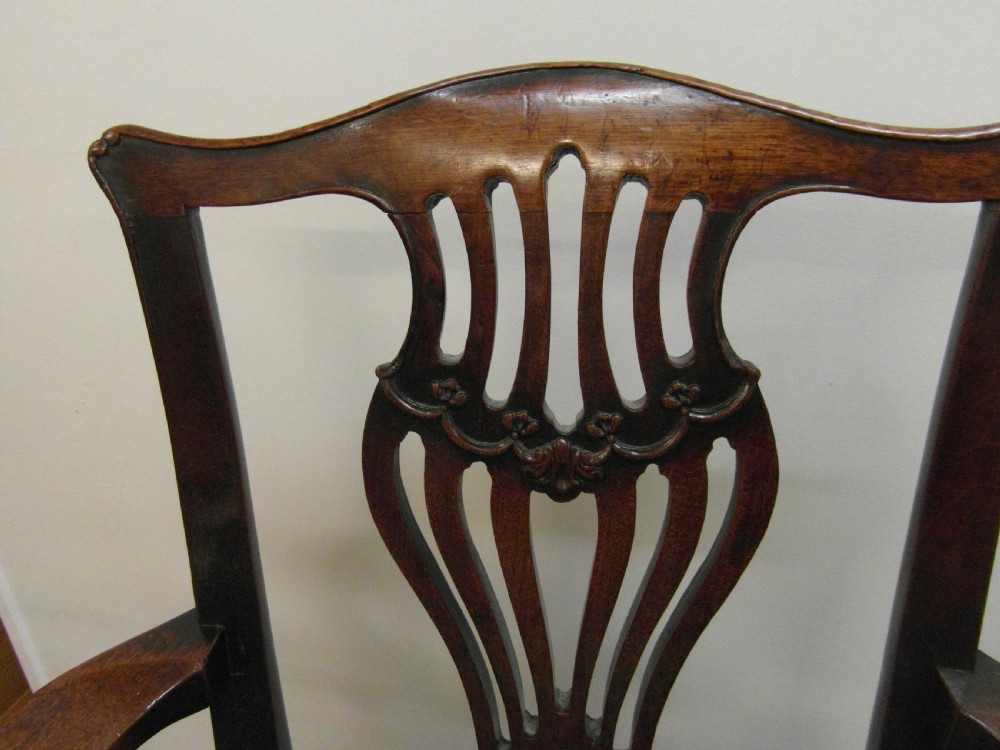 An antique Georgian mahogany childs high chair featuring a carved pierced splat back, wooden safety bar, upholstered seat, and integrated footrest on a wooden stand. View V