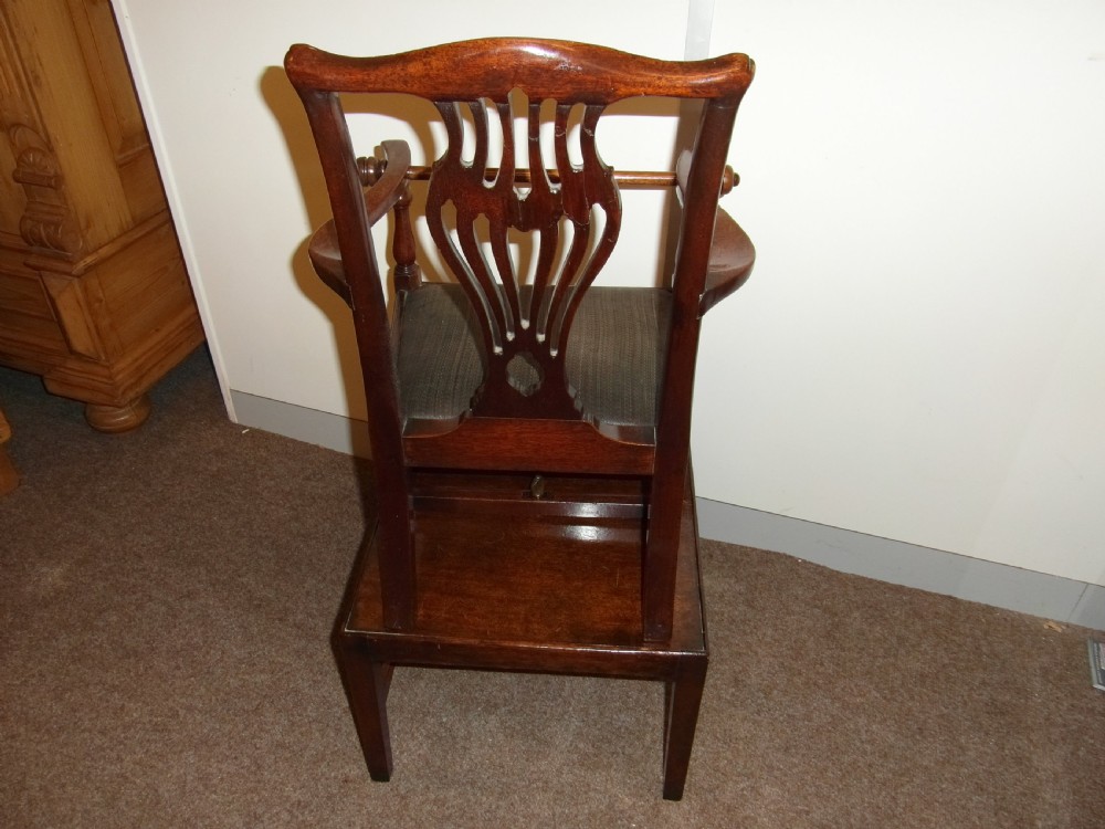 An antique Georgian mahogany childs high chair featuring a carved pierced splat back, wooden safety bar, upholstered seat, and integrated footrest on a wooden stand. View VI