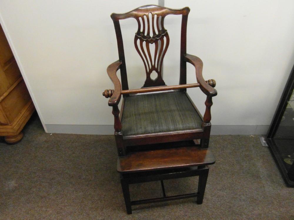 An antique Georgian mahogany childs high chair featuring a carved pierced splat back, wooden safety bar, upholstered seat, and integrated footrest on a wooden stand. View IX