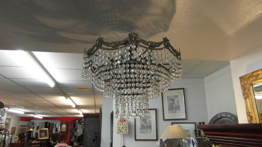 A tiered Art Deco cut glass chandelier featuring strings of crystal beads suspended from an ornate dark metal gallery with decorative scrollwork.