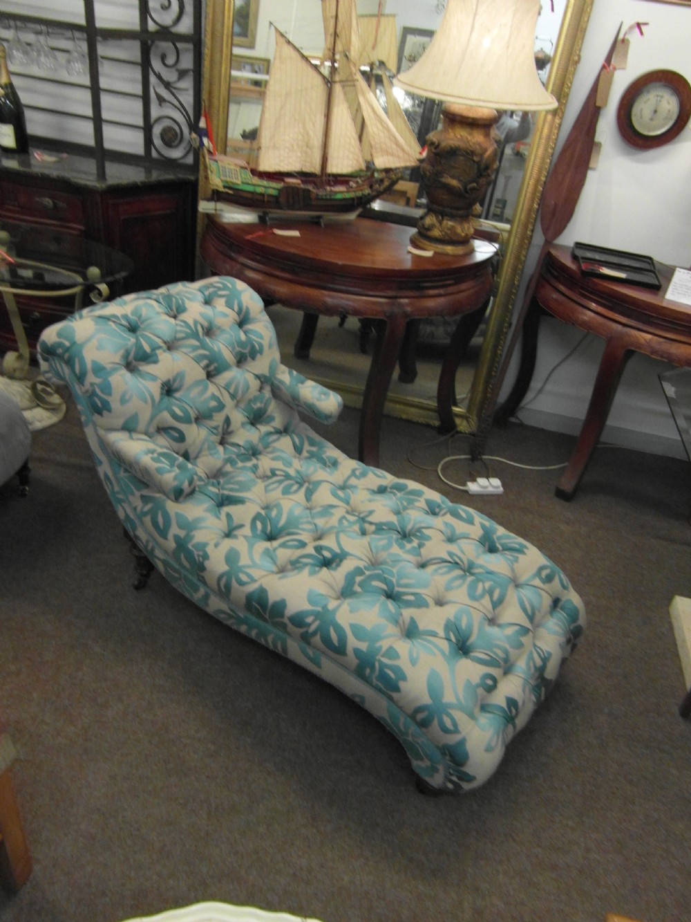 A Victorian upholstered chaise longue featuring deep-buttoned tufting in a teal and cream floral pattern with short turned wooden legs.