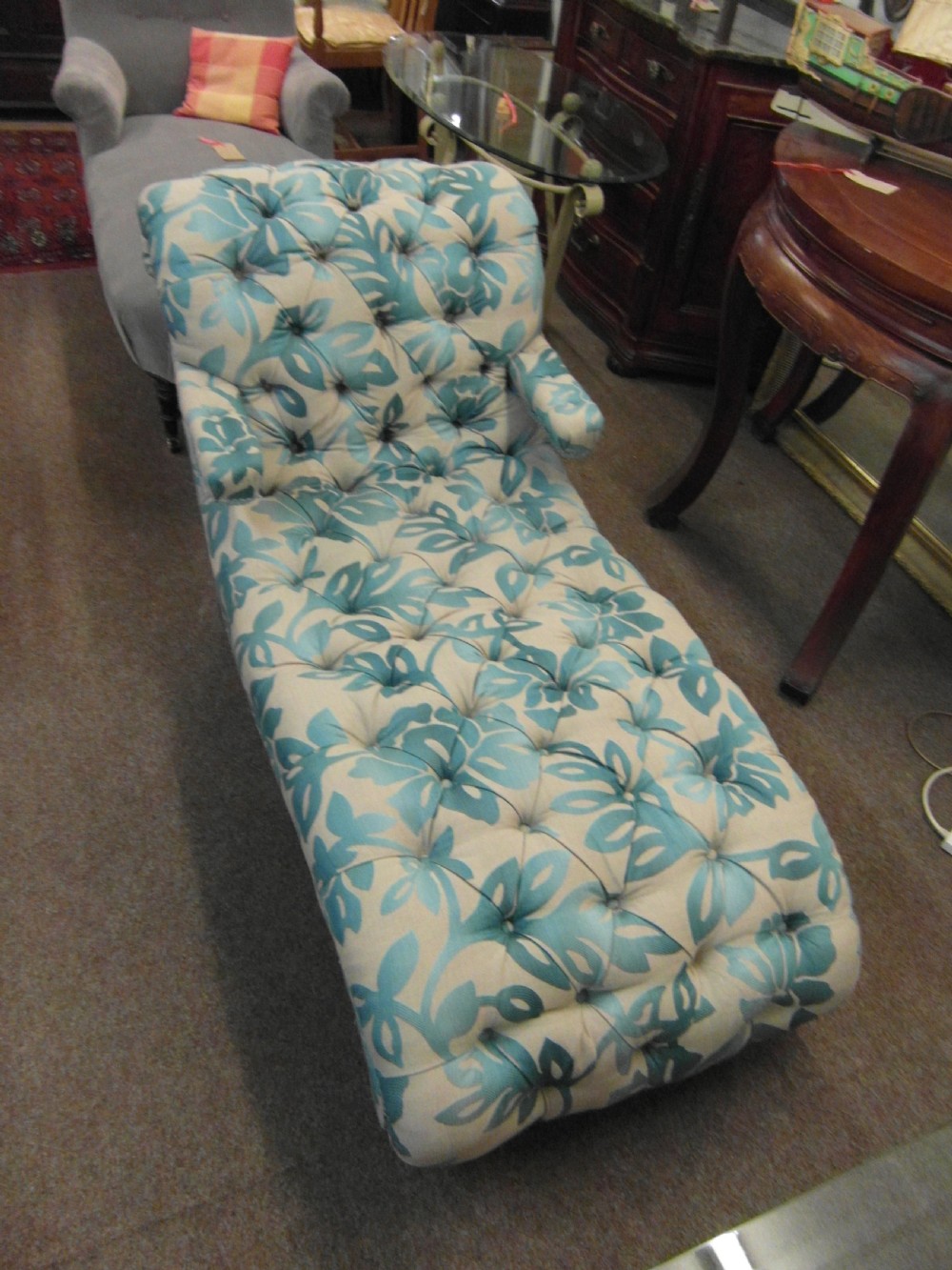 A Victorian upholstered chaise longue featuring deep-buttoned tufting in a teal and cream floral pattern with short turned wooden legs. View VI