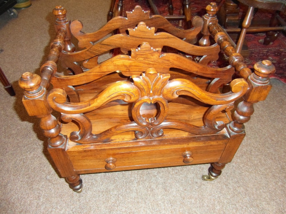 A Regency period rosewood music canterbury featuring carved scroll dividers, turned corner posts, a single base drawer with twin wooden knobs, and brass castors.