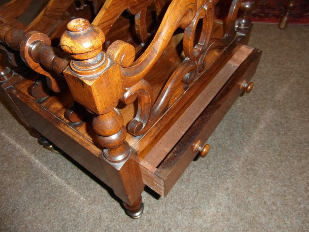A Regency period rosewood music canterbury featuring carved scroll dividers, turned corner posts, a single base drawer with twin wooden knobs, and brass castors. View III