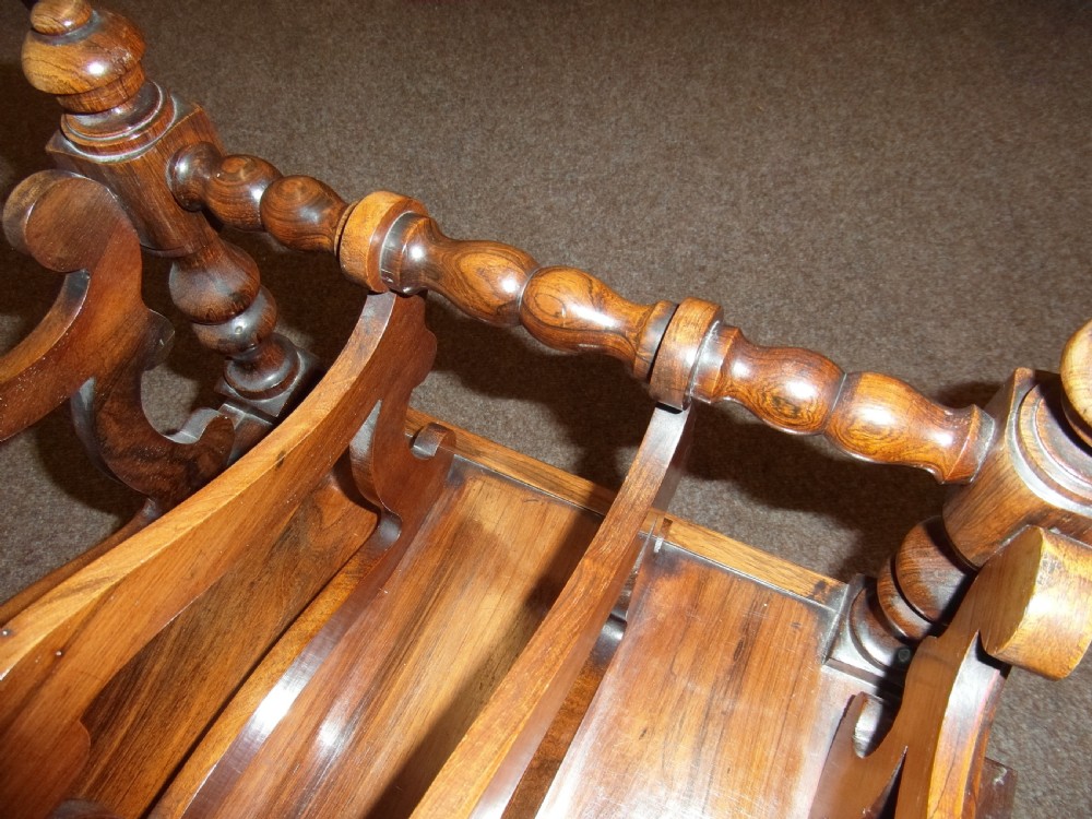 A Regency period rosewood music canterbury featuring carved scroll dividers, turned corner posts, a single base drawer with twin wooden knobs, and brass castors. View IV