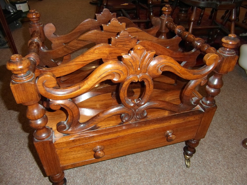 A Regency period rosewood music canterbury featuring carved scroll dividers, turned corner posts, a single base drawer with twin wooden knobs, and brass castors. View V