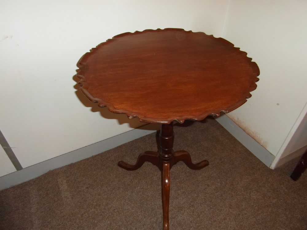 A circular dark mahogany side table featuring a carved pie-crust scalloped top supported on a turned central column and three cabriole tripod legs.