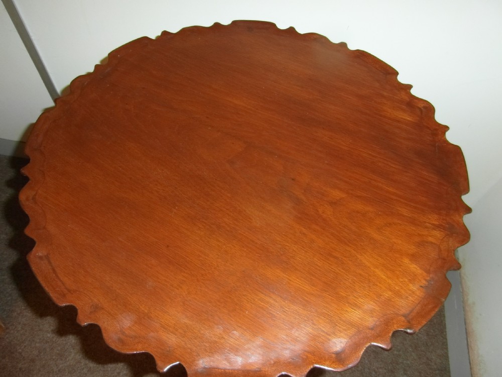 A circular dark mahogany side table featuring a carved pie-crust scalloped top supported on a turned central column and three cabriole tripod legs. View II
