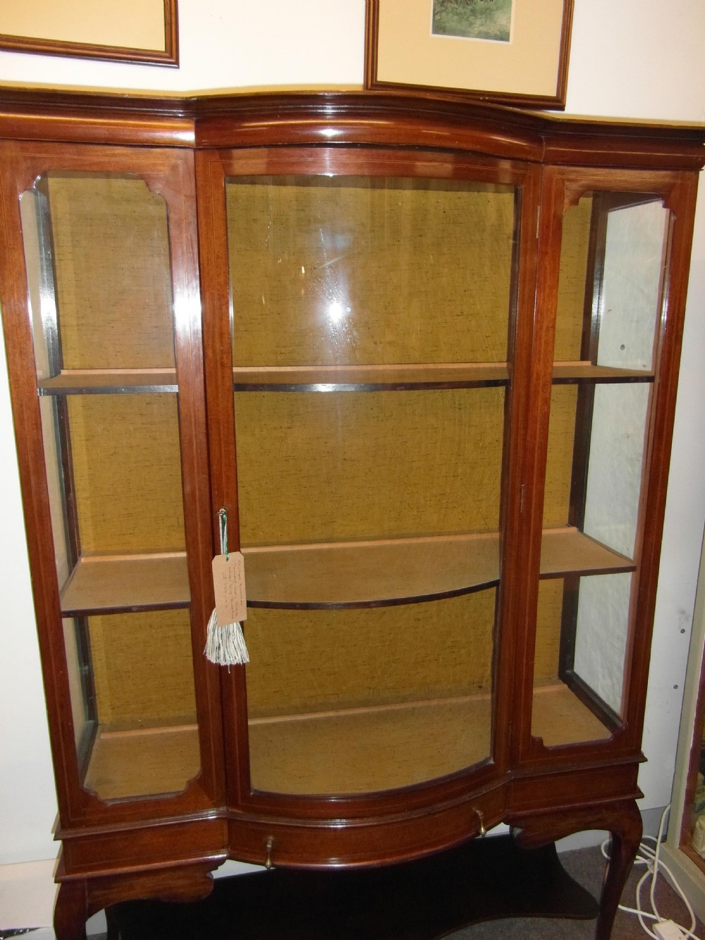 An Edwardian mahogany display cabinet featuring a bow-front glazed central section, side glass panels, interior shelves, and string inlay.