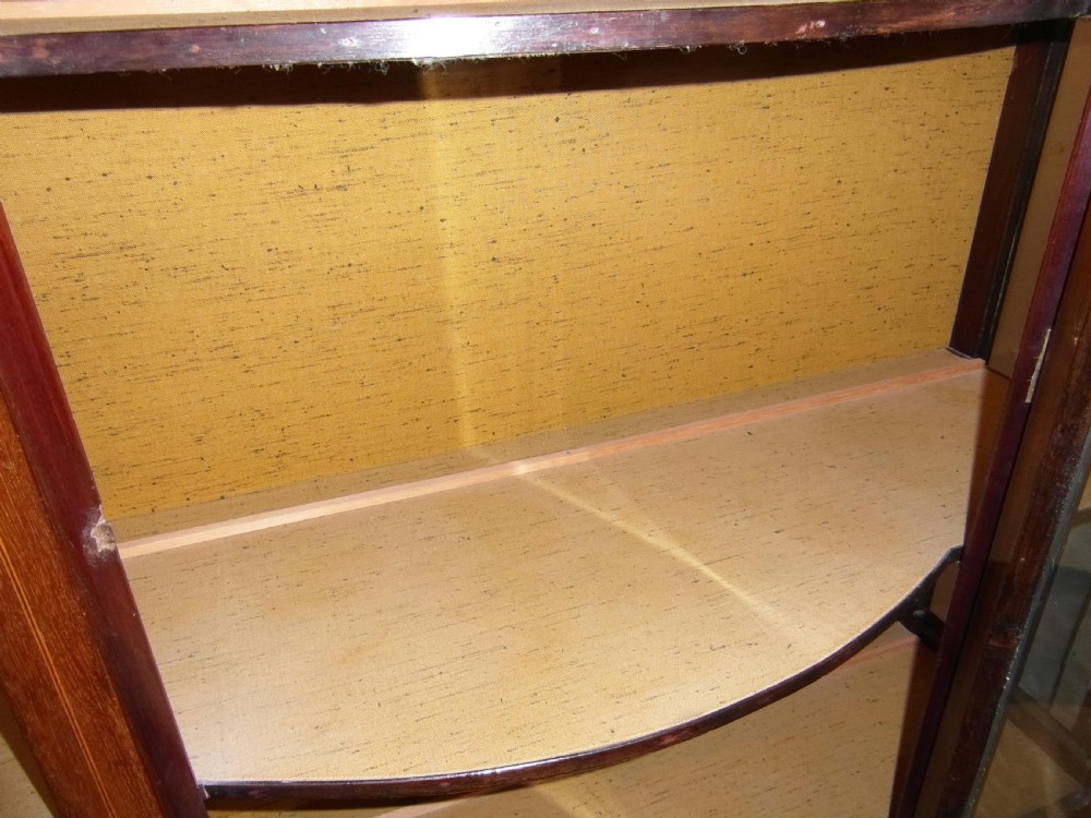 An Edwardian mahogany display cabinet featuring a bow-front glazed central section, side glass panels, interior shelves, and string inlay. View IV