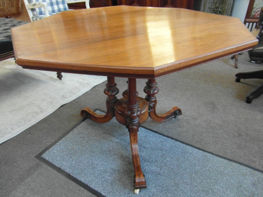 A Victorian octagonal walnut centre table with turned column supports, carved scrolled legs, and porcelain castors.