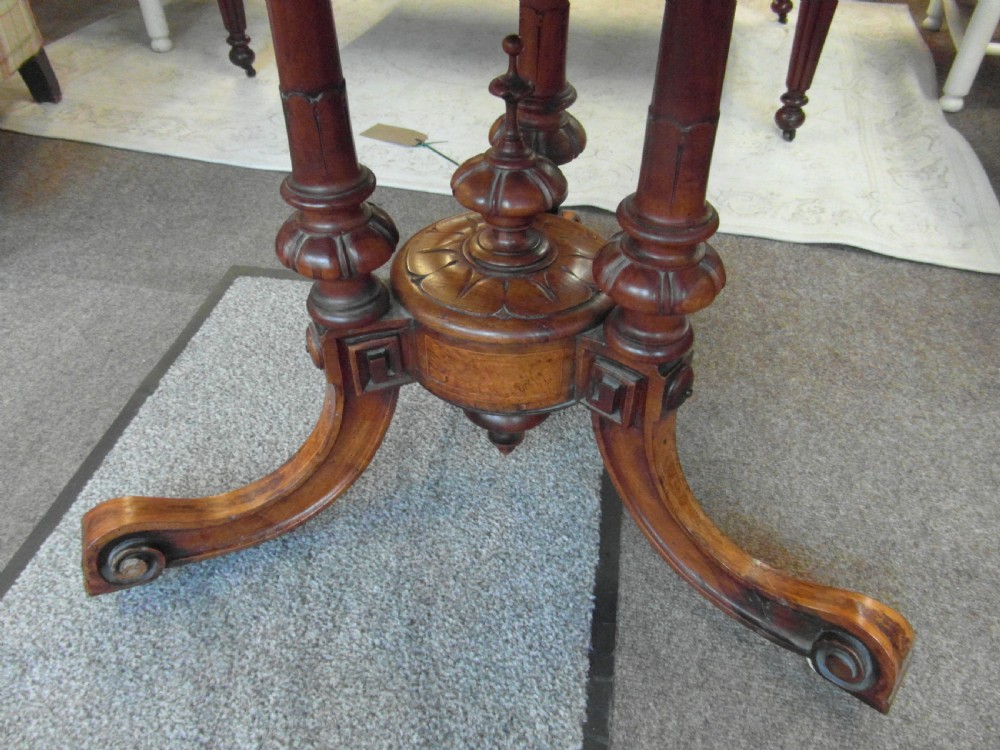 A Victorian octagonal walnut centre table with turned column supports, carved scrolled legs, and porcelain castors. View II