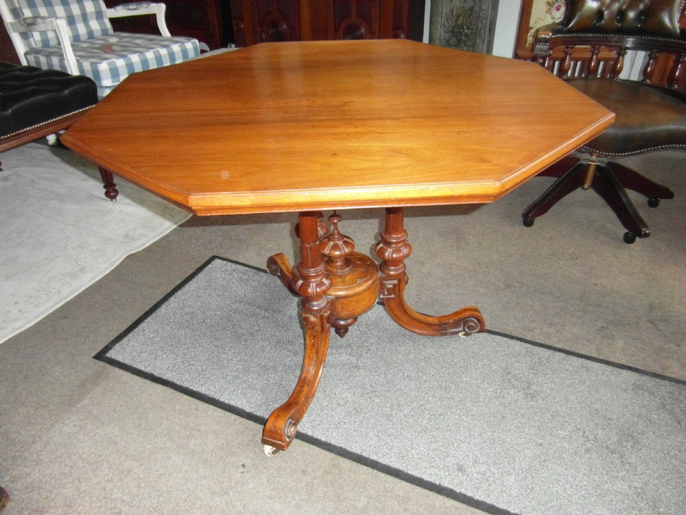 A Victorian octagonal walnut centre table with turned column supports, carved scrolled legs, and porcelain castors. View VII