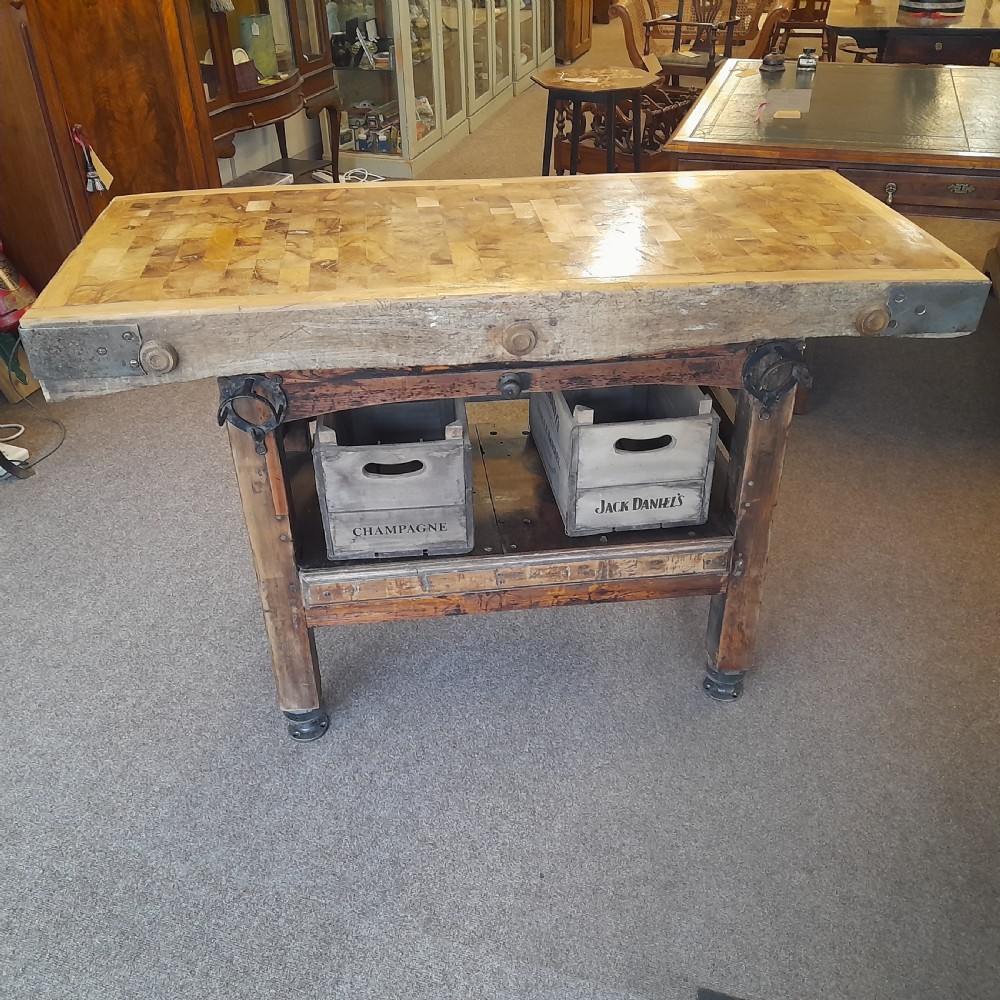 An antique butchers block featuring a thick end-grain timber top reinforced with iron corner brackets on a wooden stand with a lower shelf.