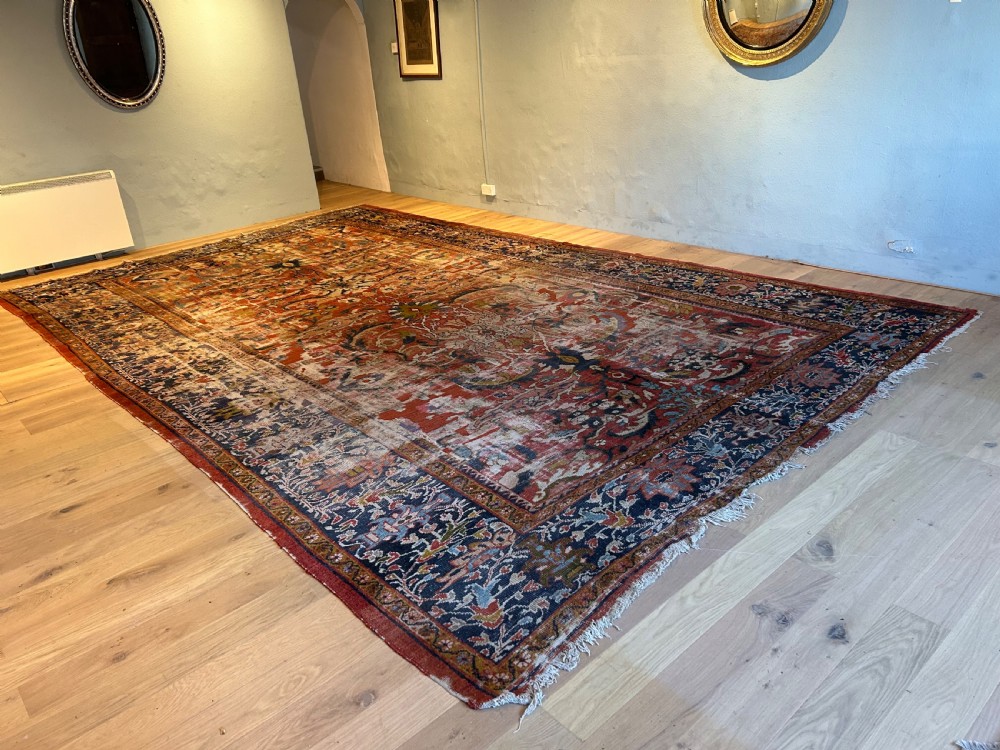 A large hand-knotted antique Ziegler carpet featuring floral palmette patterns in terracotta red, navy blue, and cream tones laid flat on a wooden floor. View II