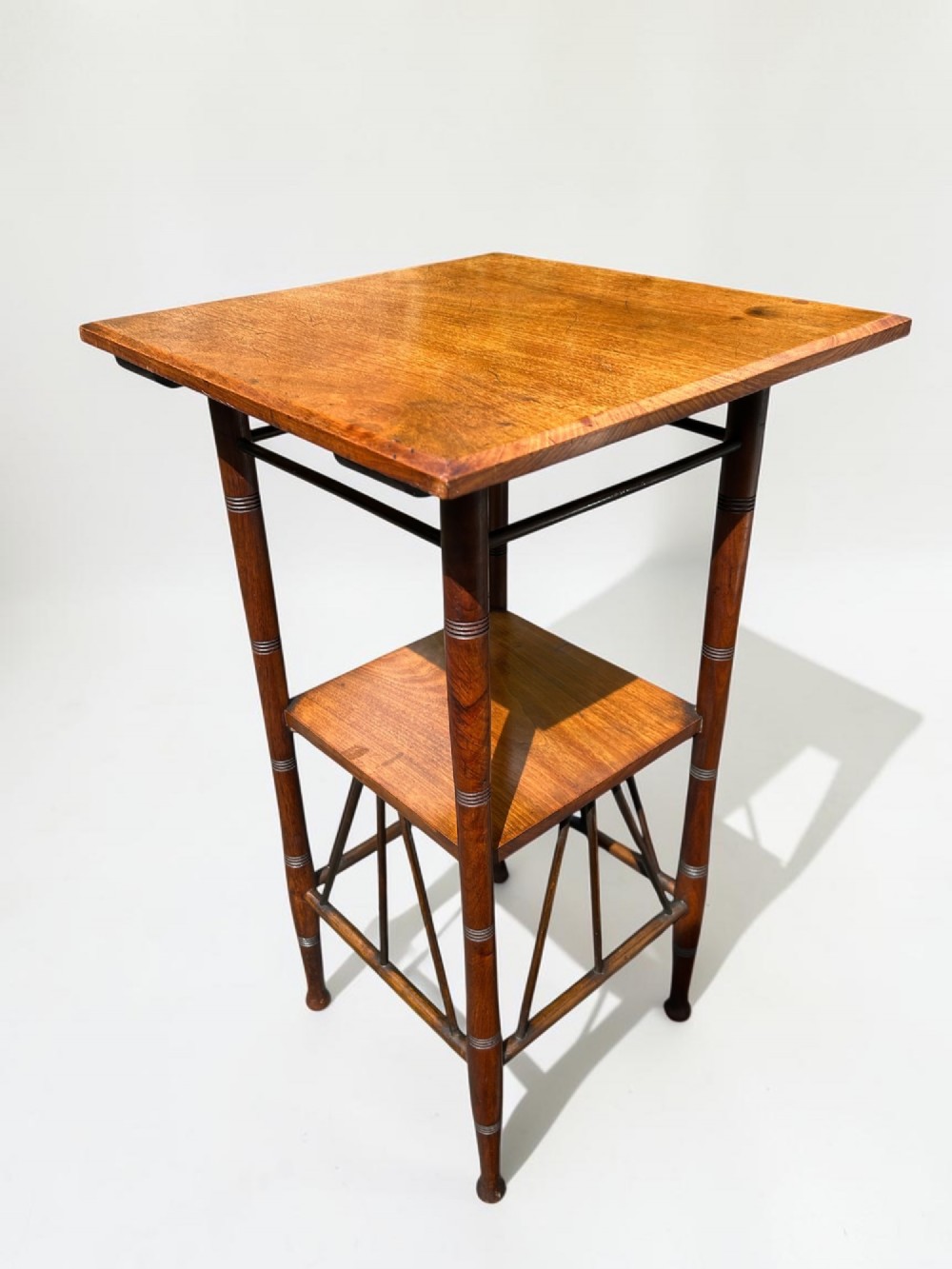 A square walnut side table in the Aesthetic Movement style featuring turned legs with incised rings, an undertier shelf, and spindled lower bracing.