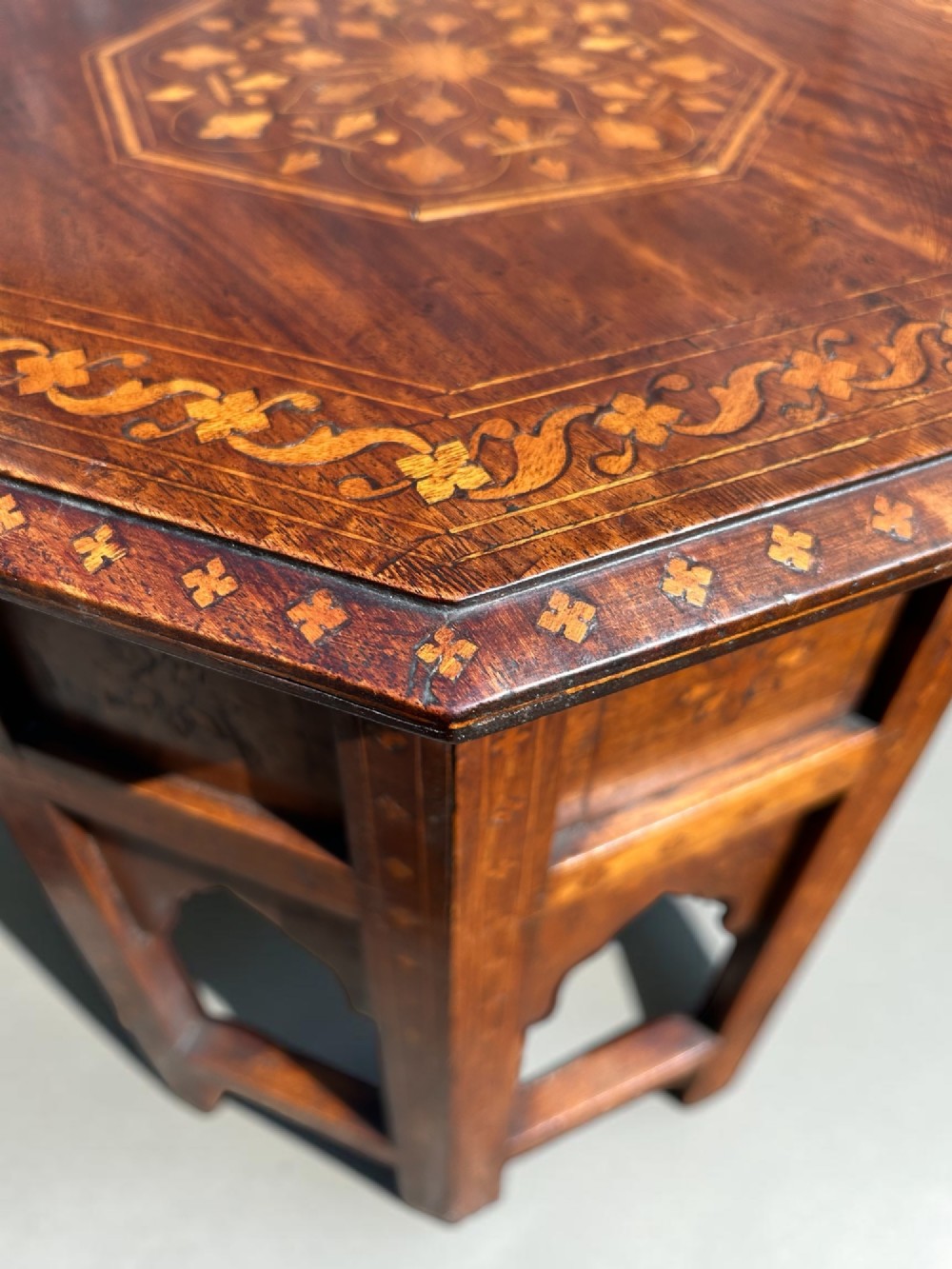 An octagonal Anglo-Indian wooden side table featuring intricate floral marquetry inlay across the top and an openwork arched apron base. View IV