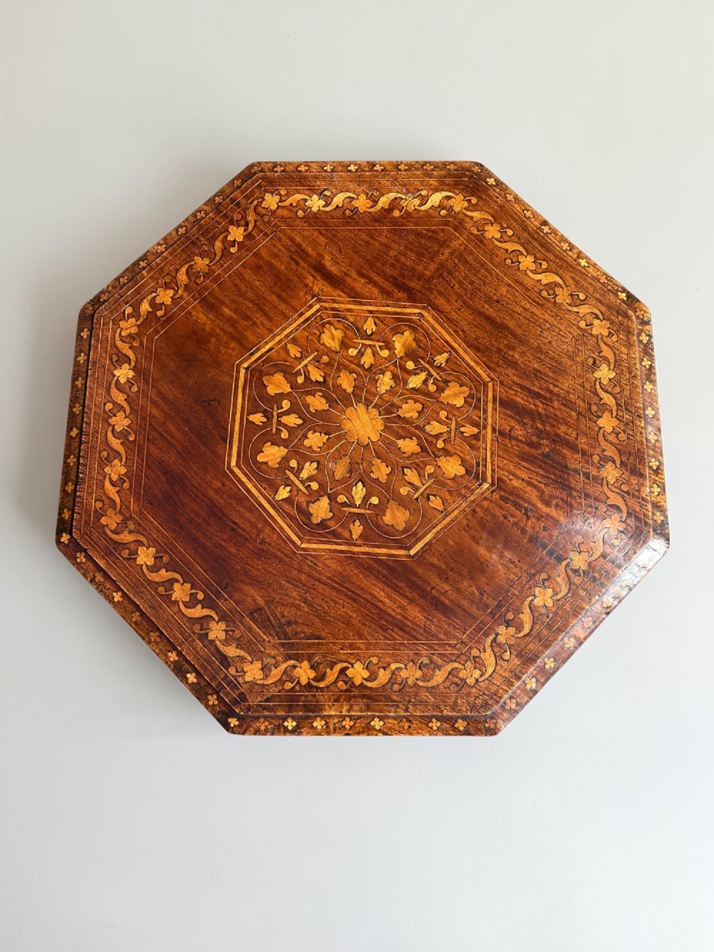 An octagonal Anglo-Indian wooden side table featuring intricate floral marquetry inlay across the top and an openwork arched apron base. View V