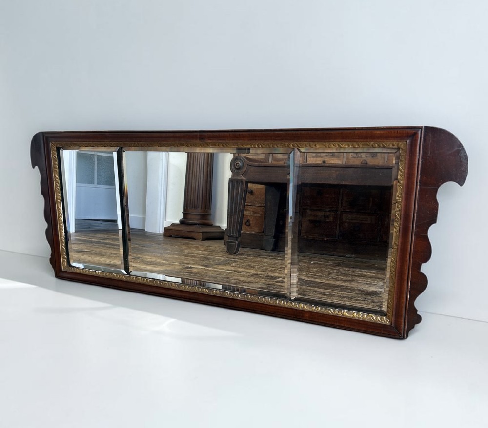 A horizontal George I walnut overmantel mirror featuring three bevelled glass plates, a gilded inner lip, and shaped side wings.