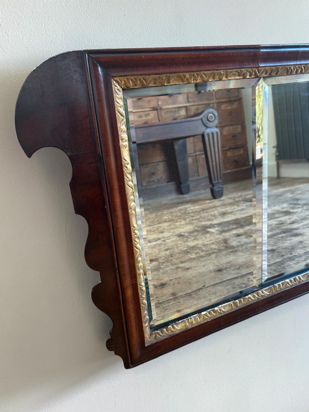 A horizontal George I walnut overmantel mirror featuring three bevelled glass plates, a gilded inner lip, and shaped side wings. View II