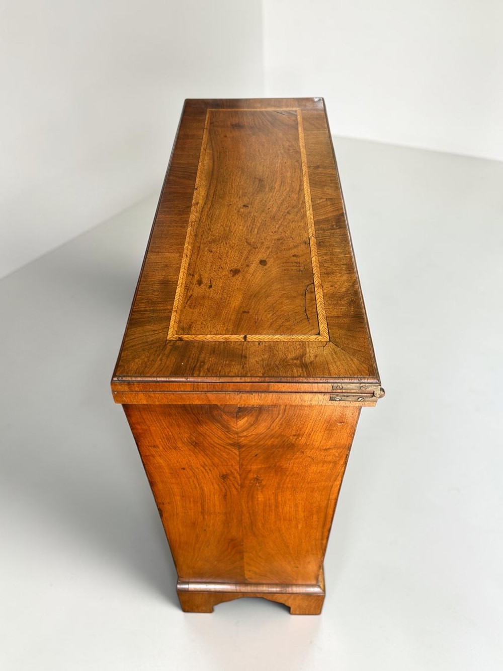 A George I walnut bachelors chest featuring four graduated drawers with feather-banded borders, brass bail handles, keyhole escutcheons, and shaped bracket feet. View III