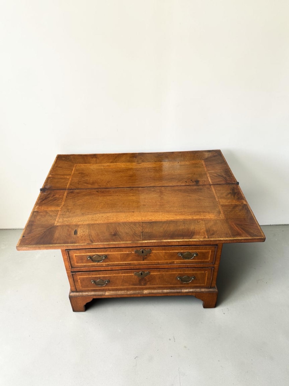 A George I walnut bachelors chest featuring four graduated drawers with feather-banded borders, brass bail handles, keyhole escutcheons, and shaped bracket feet. View IV