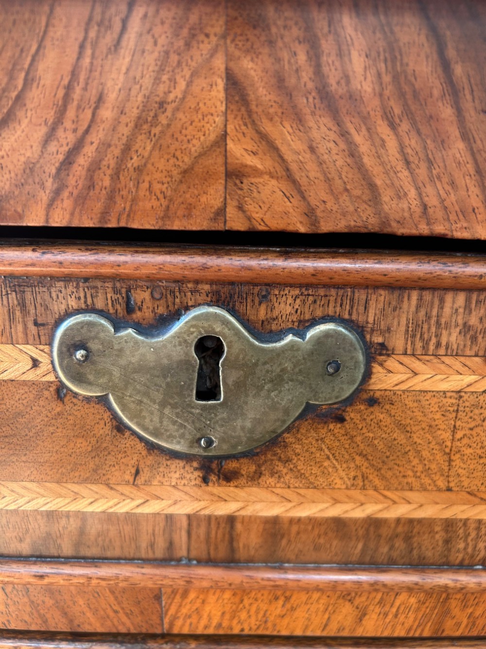 A George I walnut bachelors chest featuring four graduated drawers with feather-banded borders, brass bail handles, keyhole escutcheons, and shaped bracket feet. View V