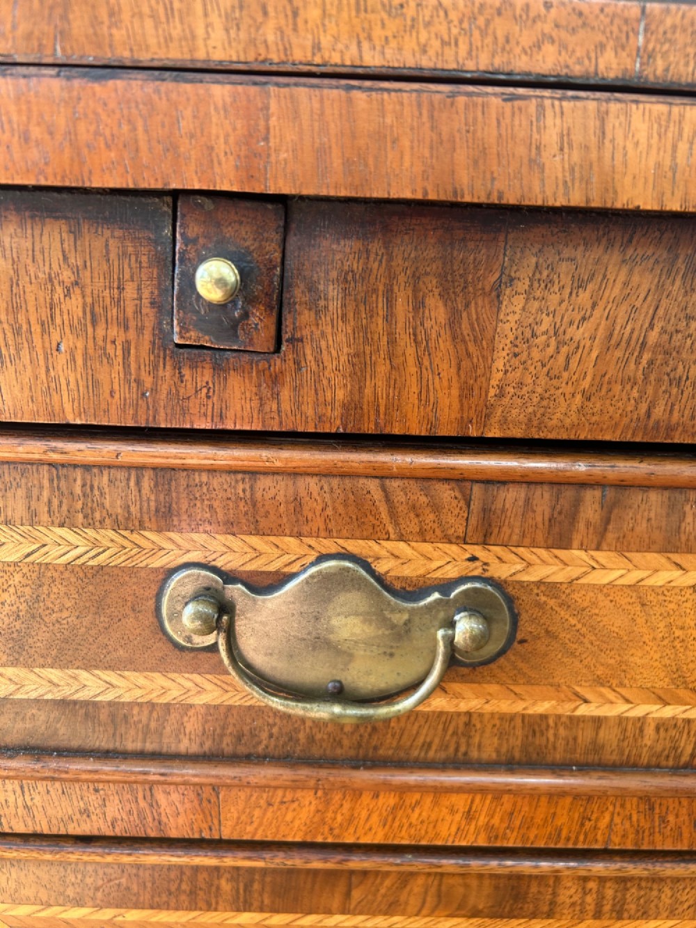 A George I walnut bachelors chest featuring four graduated drawers with feather-banded borders, brass bail handles, keyhole escutcheons, and shaped bracket feet. View VI