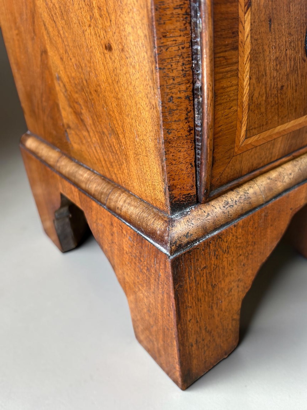 A George I walnut bachelors chest featuring four graduated drawers with feather-banded borders, brass bail handles, keyhole escutcheons, and shaped bracket feet. View VII