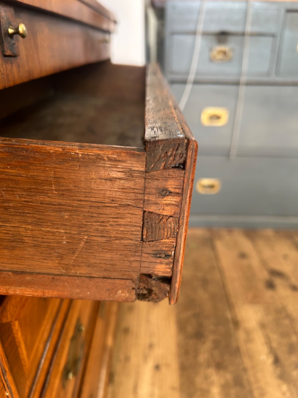 A George I walnut bachelors chest featuring four graduated drawers with feather-banded borders, brass bail handles, keyhole escutcheons, and shaped bracket feet. View VIII