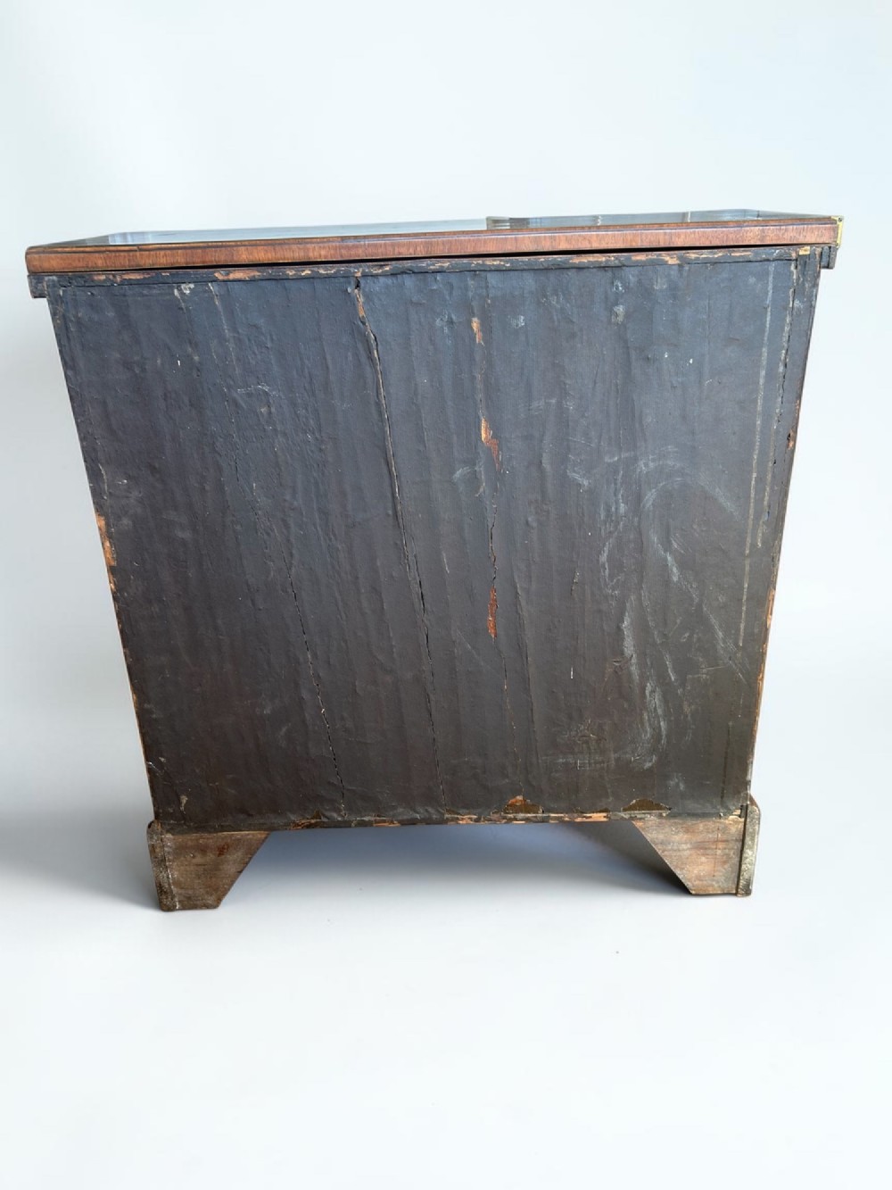 A George I walnut bachelors chest featuring four graduated drawers with feather-banded borders, brass bail handles, keyhole escutcheons, and shaped bracket feet. View X