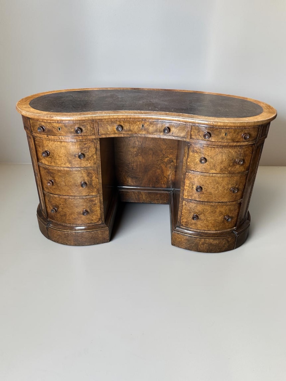 A 19th-century freestanding kidney-shaped desk crafted from warm brown burr walnut with a dark leather inset top and dual drawer pedestals.