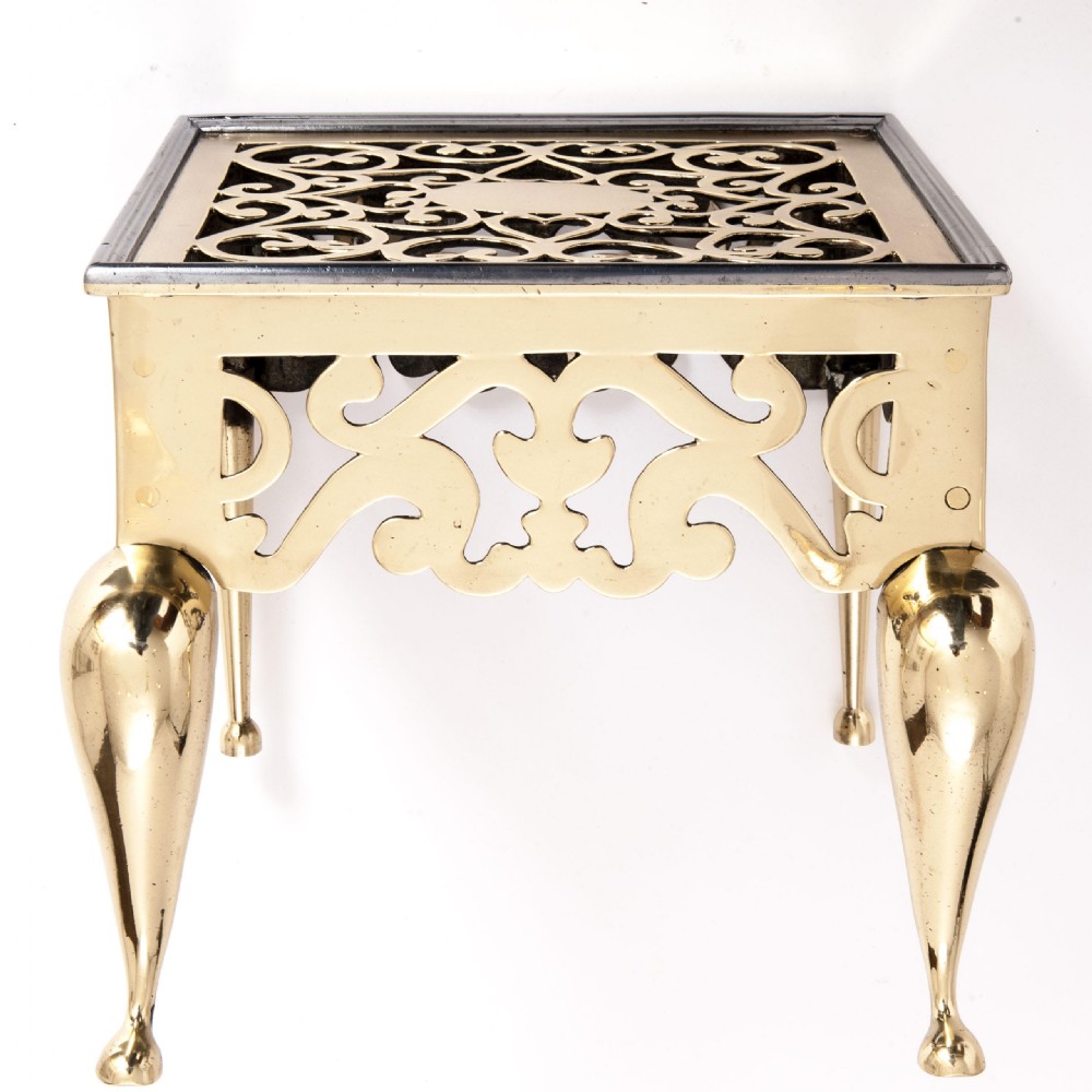 An antique brass fireplace footman with decorative pierced fretwork on the top and apron, supported by curved cabriole legs.