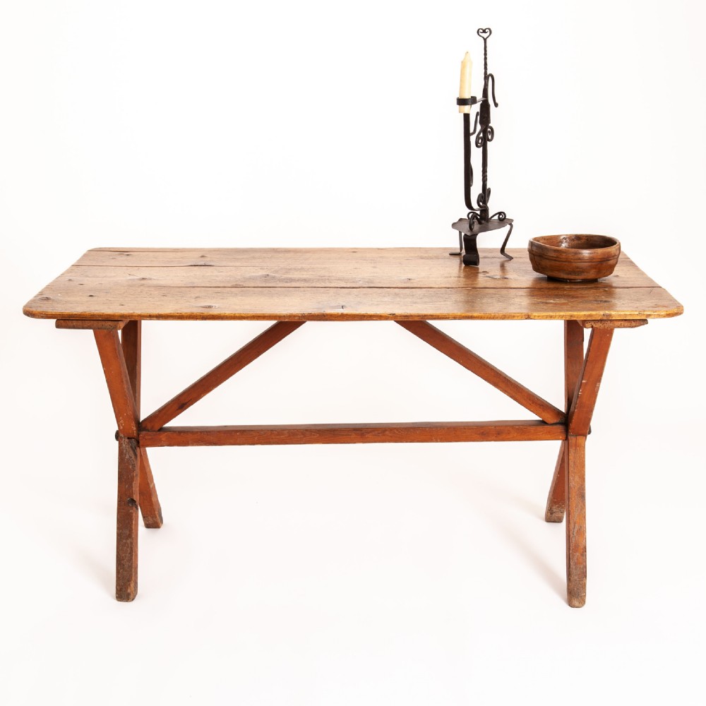 A rustic pine tavern table featuring a rectangular planked top supported by crossed legs and diagonal bracing stretchers.