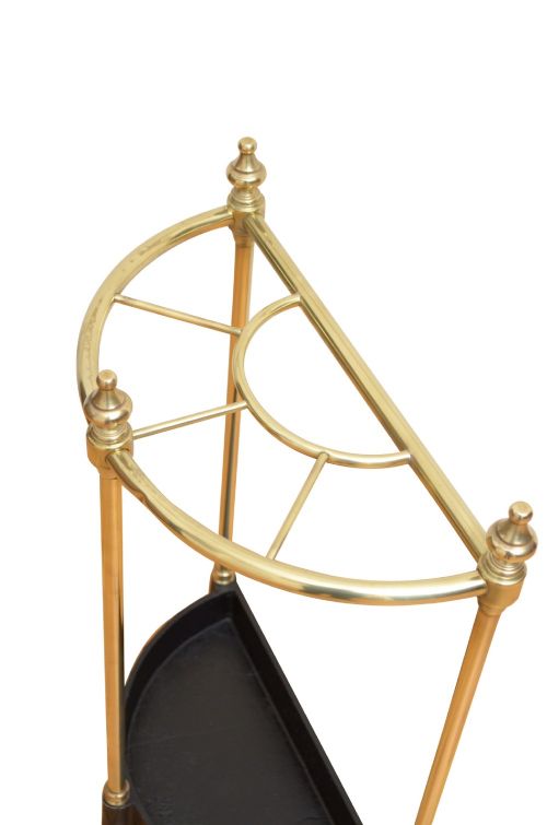 An Edwardian brass umbrella stand featuring a demi-lune frame, urn finials, three vertical posts, and a black cast iron drip tray with a dogtooth pattern. View V