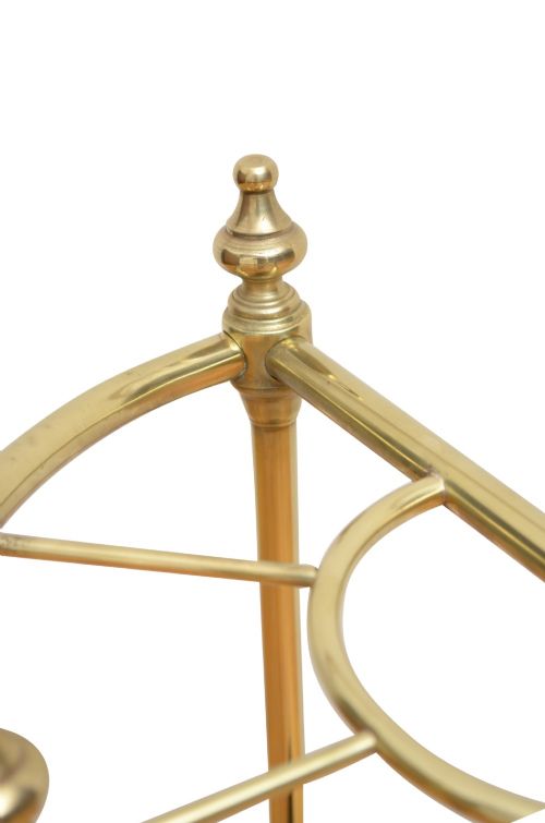 An Edwardian brass umbrella stand featuring a demi-lune frame, urn finials, three vertical posts, and a black cast iron drip tray with a dogtooth pattern. View VI