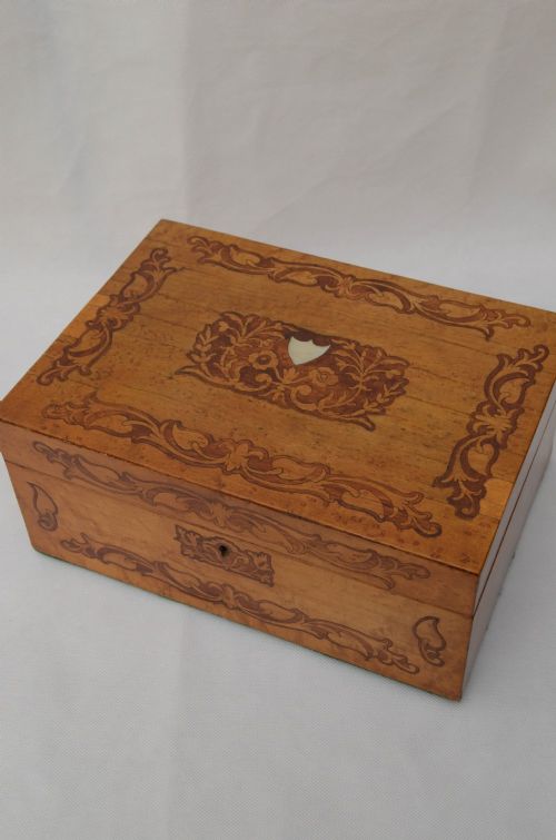 An open Victorian birds eye maple wooden box featuring scrollwork tulipwood inlay on the front and a green patterned paper interior lining. View II