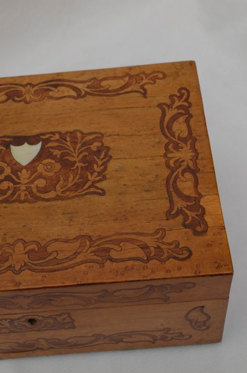 An open Victorian birds eye maple wooden box featuring scrollwork tulipwood inlay on the front and a green patterned paper interior lining. View V