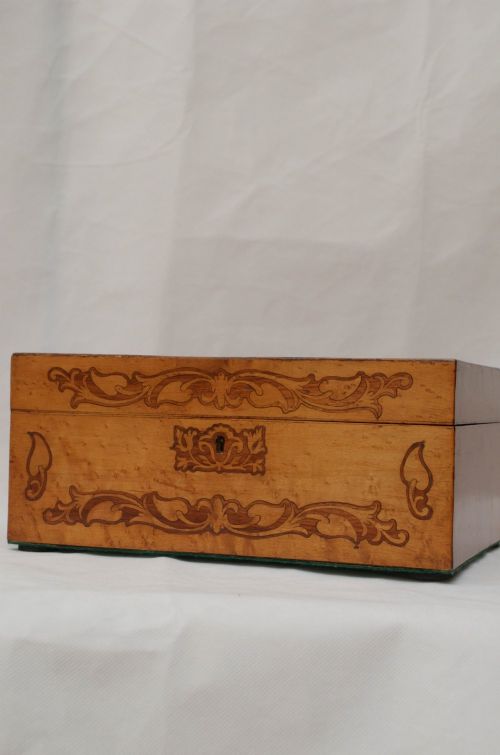 An open Victorian birds eye maple wooden box featuring scrollwork tulipwood inlay on the front and a green patterned paper interior lining. View VI