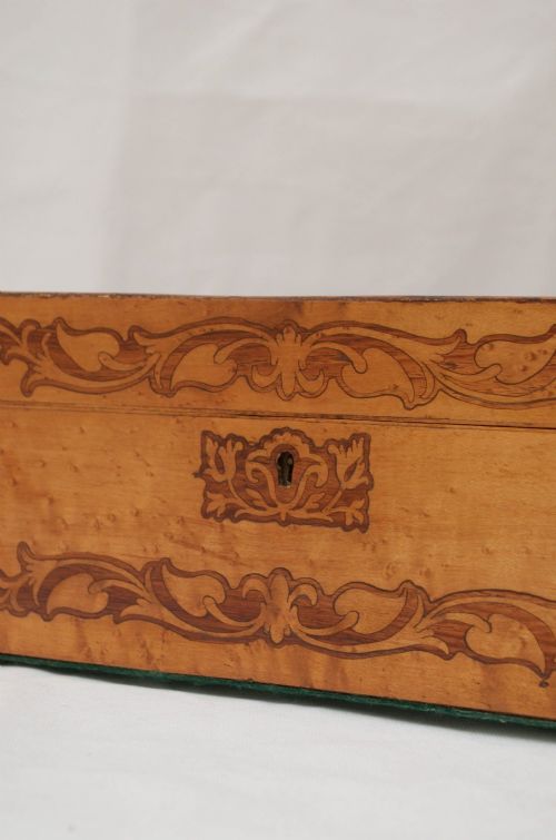 An open Victorian birds eye maple wooden box featuring scrollwork tulipwood inlay on the front and a green patterned paper interior lining. View VII