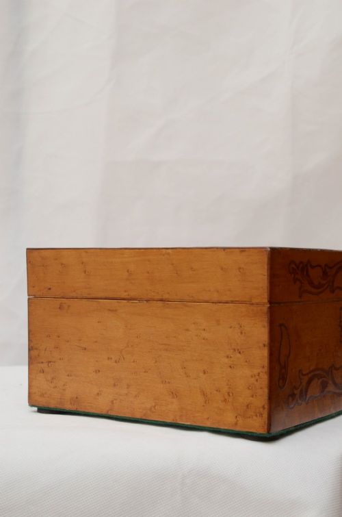 An open Victorian birds eye maple wooden box featuring scrollwork tulipwood inlay on the front and a green patterned paper interior lining. View X