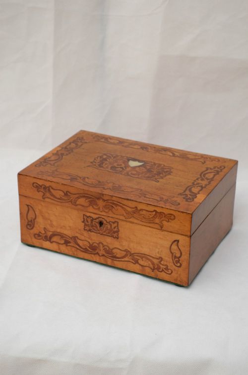 An open Victorian birds eye maple wooden box featuring scrollwork tulipwood inlay on the front and a green patterned paper interior lining. View XIII