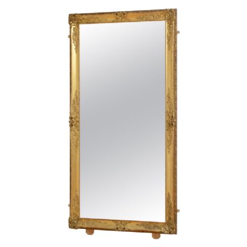 A large rectangular full-length mirror featuring an ornate gold leaf frame leaning against a neutral wall. View II