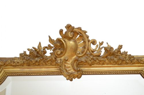 A large nineteenth-century French giltwood overmantel mirror featuring an ornate carved cresting motif and a arched top rectangular frame. View III