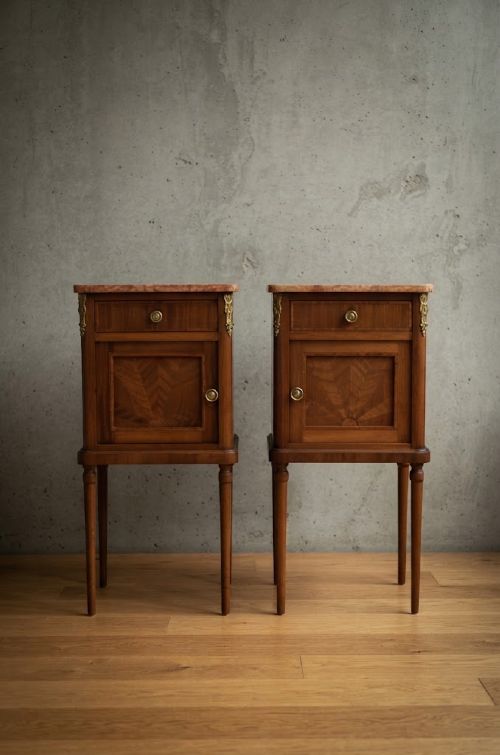 A matching pair of French mahogany bedside cabinets featuring pink marble tops, single drawers over small cupboards with sunburst parquetry, and slender turned legs. View XV