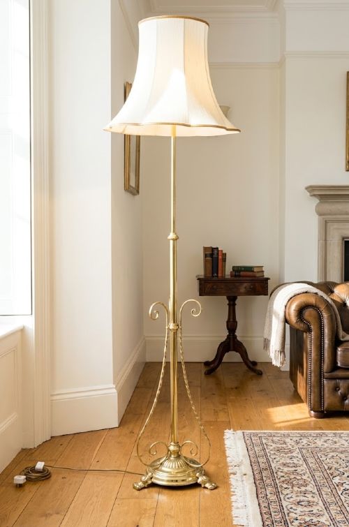 An English Arts and Crafts brass standard lamp featuring a telescopic height-adjustable stem, ornamental scroll braces, a fluted circular base, and a flared white fabric shade. View II