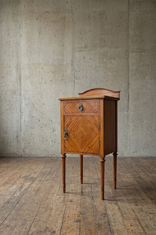 An antique satinwood bedside cupboard featuring a shaped gallery back, top drawer, chevron parquetry cupboard door, and slender fluted legs. View III