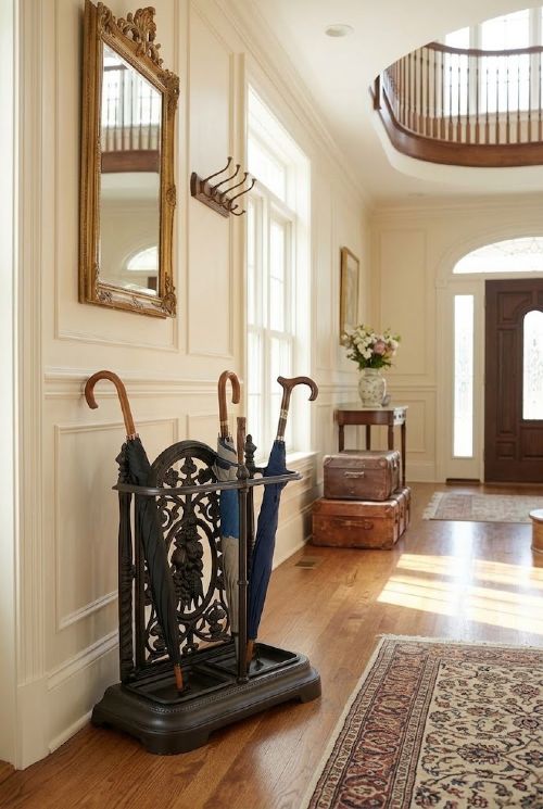 A black cast iron umbrella stand featuring an ornate foliate backplate, top support rail, and a twin-section drip tray at the base. View III