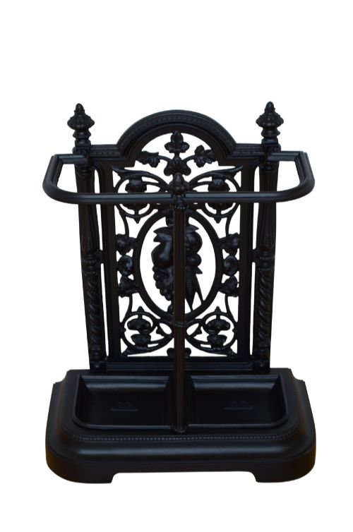 fig 1. A black cast iron umbrella stand featuring an ornate foliate backplate, top support rail, and a twin-section drip tray at the base.